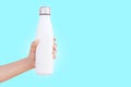 Close-up of female hand holding white reusable steel thermo water bottle isolated on background of cyan color with copy space. Royalty Free Stock Photo