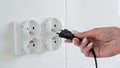 Close-up of a female hand inserting a black electric plug into a double European electrical socket  on a white wall. Royalty Free Stock Photo