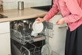 Close-up of female hand loading wished to, empty out or unloading from open automatic built-in dishwashers machine with clean Royalty Free Stock Photo