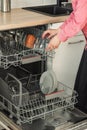 Close-up of female hand loading wished to, empty out or unloading from open automatic built-in dishwashers machine with clean Royalty Free Stock Photo