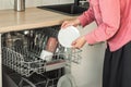 Close-up of female hand loading wished to, empty out or unloading from open automatic built-in dishwashers machine with clean Royalty Free Stock Photo