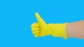 Close up of female hand in yellow protective latex rubber glove showing thumbs up sign, gesture against blue background