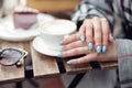 Close up of female hands with blue manicure and cup of coffee at cafe. Cappuccino time.