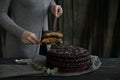 Woman cuts chocolate cake close. Dark tones