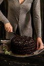 Woman cuts chocolate cake close. Dark tones