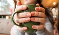 Close up of female hands with a drink mug. A girl in a gray sweater holds a cup of coffee or cocoa in a cafe at the table and Royalty Free Stock Photo