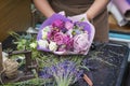 Close-up of female hands of florist creating fashionable modern romantic bouquet of different flowers on table in shop