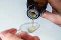 Close-up of female hands holding a bottle of expectorant cough syrup and pouring it with a measuring spoon.