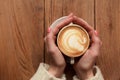 Close-up female hands holding cup with coffee cappuccino with foam with nice pattern. Perfect red gel polish manicure. Wood