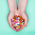 Close up of female hands holding heap of colorful medication pills over pastel blue background.