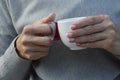 A woman in a gray sweater holds a white cup of tea or coffee. Close-up of female hands with a cup Royalty Free Stock Photo