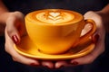 Close up of female hands holding a yellow coffee cup with latte art