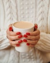 Close-up of female hands with a mug of beverage. Girl in warm sweater is holding hot cup of coffee or cocoa in hands. Royalty Free Stock Photo