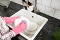 Close up of female hands in pink protective rubber gloves washing white plate with purple cleaning sponge Royalty Free Stock Photo