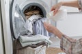 Close up of female hands pouring liquid laundry detergent into cap. Washer machine and clothes with wicker basket in background Royalty Free Stock Photo