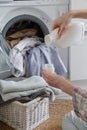 Close up of female hands pouring liquid laundry detergent into cap. Washer machine and clothes with wicker basket in background Royalty Free Stock Photo