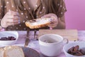 Female hands spreading delicious jam on a slice of bread over a table with bread, cutlery, a cutting board and a plate of dates. Royalty Free Stock Photo