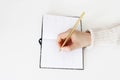 Close-up of female hands in sweater holding golden balpoint pen and writing on open notebook on white table background Royalty Free Stock Photo