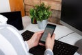 Close-up of female hands using modern smart phone while working at office with computer, businesswoman typing text message on her