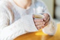 Close-up of female hands in a warm sweater holding a white Cup of hot coffee or tea in a coffee shop. The concept of winter comfor