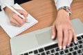 Close-up of female hands writing in notepad and typing on laptop keyboard Royalty Free Stock Photo