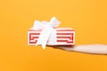 Close up female hold in hand red white striped present gift box with ribbon bow isolated on trending yellow orange Royalty Free Stock Photo