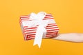 Close up female hold in hand red white striped present gift box with ribbon bow isolated on trending yellow orange Royalty Free Stock Photo