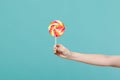 Close up female holding in hand colorful round lollipop isolated on blue turquoise wall background. Proper nutrition or