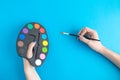 Close up of female holding paint palette and brush isolated on blue.