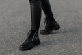 Close up of female legs in fashionable leather black boots. Urban girl in stylish leggings in trendy shoes walks on the asphalt on Royalty Free Stock Photo