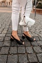 Close-up of female legs in white jeans in fashionable black leather summer shoes with a stylish bag on the street Royalty Free Stock Photo