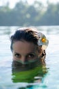 Close up of a female model face, half in the water of a pool with a tropical flower in a hear and jungles in the background Royalty Free Stock Photo