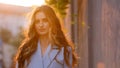 Close-up female model pensive beautiful girl with long curly blonde hair stands outside sunbeams sunset background Royalty Free Stock Photo