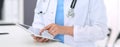 Unknown doctor woman at work. Female physician using digital tablet while standing near reception desk at clinic or