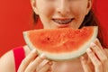 A close-up of a female teenager mouth with dental braces and a piece of delicious watermelon. The smile of a cute teen girl eating