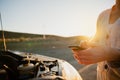 Close up of female using smartphone researching steps to fixing broken down car standing on highway. Royalty Free Stock Photo