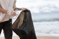 Close up of female volunteer collecting bottles from the coastal zone in plastic trash bag, free space Royalty Free Stock Photo