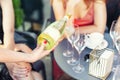 Close-up female waiter holding bottle of white champagne or prosecco at outdoor party on bright summer day. Girls hen-party Royalty Free Stock Photo