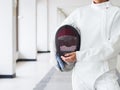 Close-up of a fencer in white fencing suit and holding mask on g