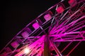 Close up of a bright pink ferris wheel lit up against a dark sky during a festival in a city Royalty Free Stock Photo