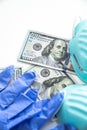 A close up of a few hundred dollar bills or cash laying below blue ribbed medical masks and pair of worn used latex gloves for