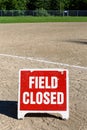 Close up of Field Closed sign on empty local baseball field, third base and baseline, on a sunny day with woods in the background Royalty Free Stock Photo