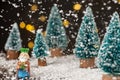 Close-up of figure of the Magus King Melchior with artificial Christmas trees, snow falling, on wooden table with snow, selective