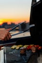 Close-up of filet mignon vegetables and meat on a bbq grill on a skyscraper rooftop at sunset. Fire in the barbecue