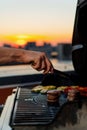 Close-up of filet mignon vegetables and meat on a bbq grill on a skyscraper rooftop at sunset. Fire in the barbecue