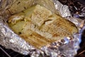 Close up fillet of white fish in the foil, sprinkled with black pepper and aromatic herbs, on a baking sheet removed from the oven