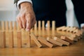 Close up finger businessman stopping wooden block from falling in the line of domino with risk concept Royalty Free Stock Photo