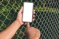 Close-up. Finger in front of a smartphone mockup in the hands of a man. Against the background of a steel wire fence and nature Royalty Free Stock Photo