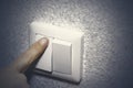 Close up. A finger presses down on a single white light switch on a wall. COPY SPACE Royalty Free Stock Photo