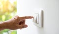 Finger pressing a white light switch on a textured wall with blurred green foliage background Royalty Free Stock Photo